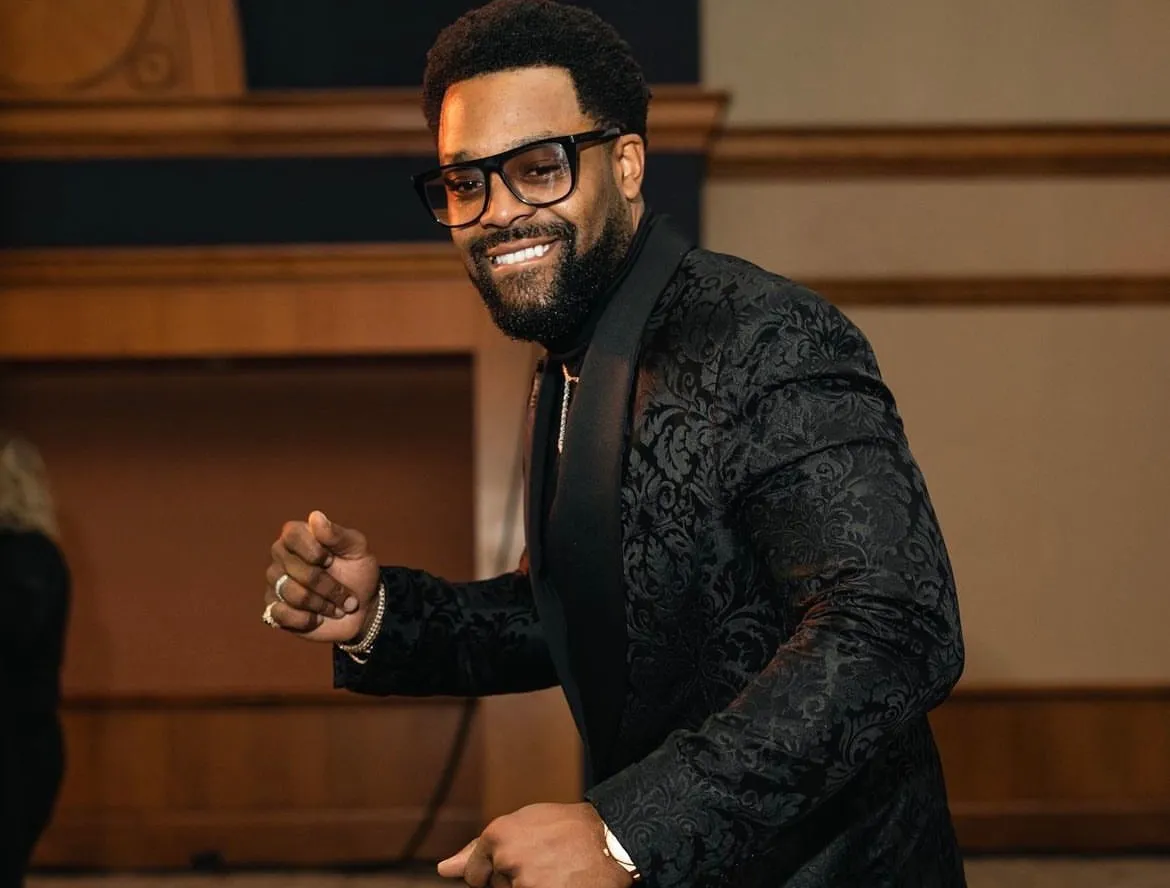 LaRoyce Hawkins in a black sequined jacket hosting on stage, mid-gesture