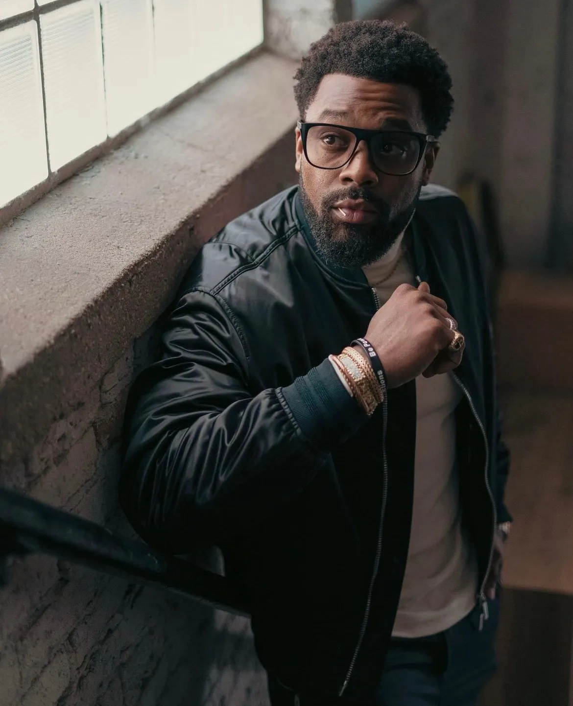 LaRoyce in a black leather jacket and glasses by a window